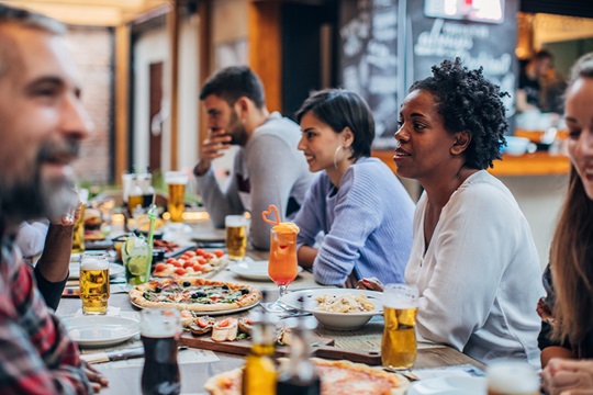 Eine Gruppe von Menschen sitzt gemeinsam an einem Tisch in einem Restaurant; mehrere Unterhaltungen.