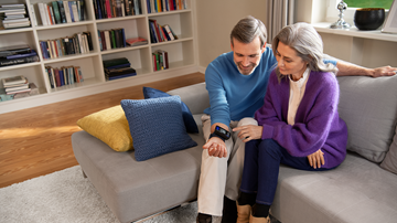 A couple sitting comfortably on a sofa with a health-monitoring device, surrounded by a cozy home library.