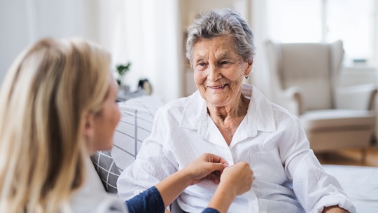 Pflegerin knöpft Seniorin die Bluse zu