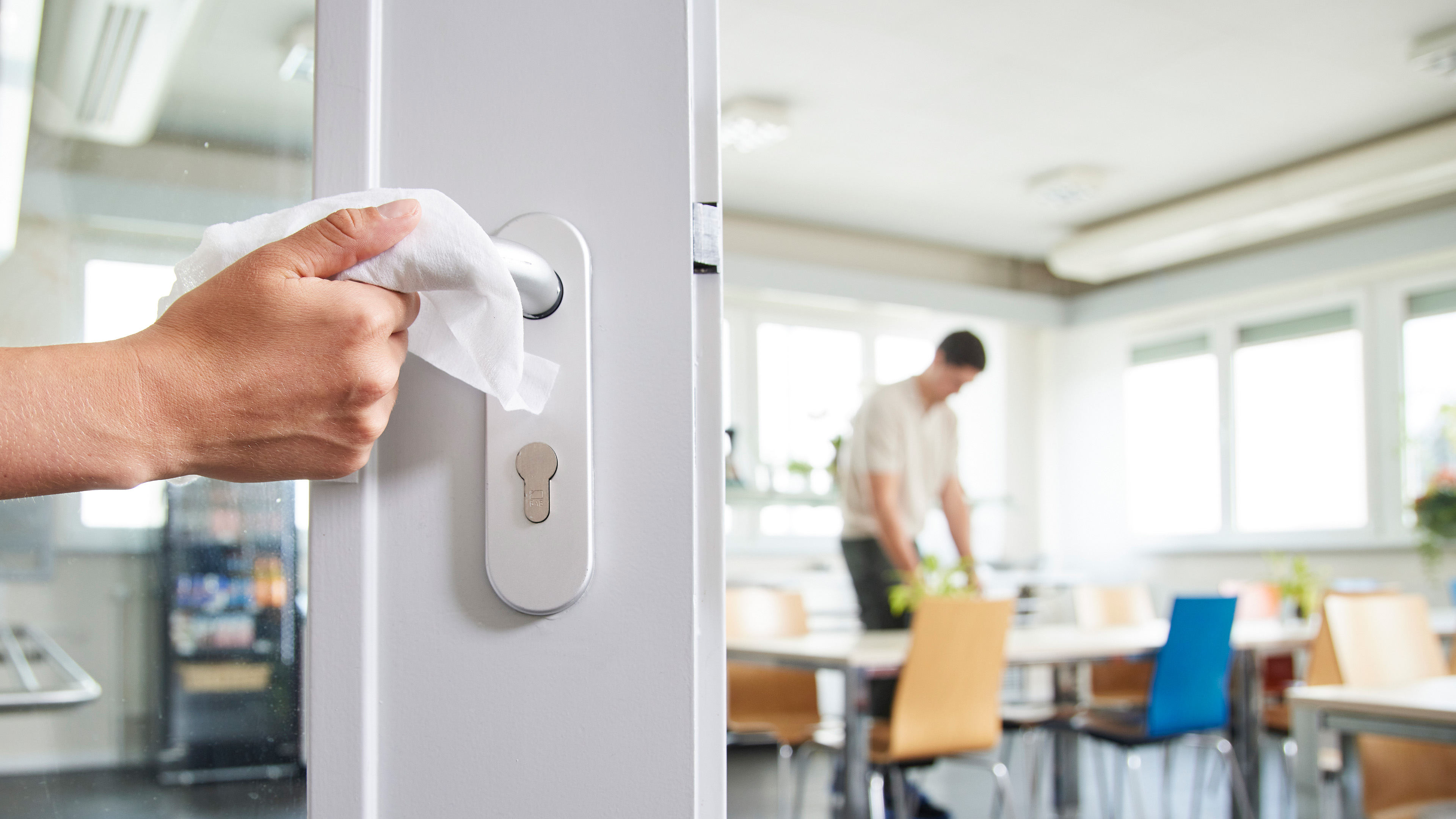 Hand wischt an einer Bürotüre den Griff mit Desinfektionstuch ab