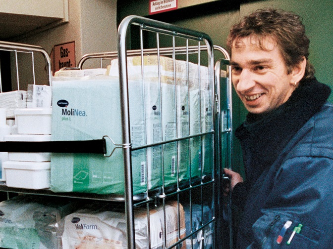 Mann schiebt Rollcontainer mit Inkontinenzprodukten ins Lager