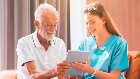 Pflegefachkraft zeigt Senior etwas auf einem Tablet