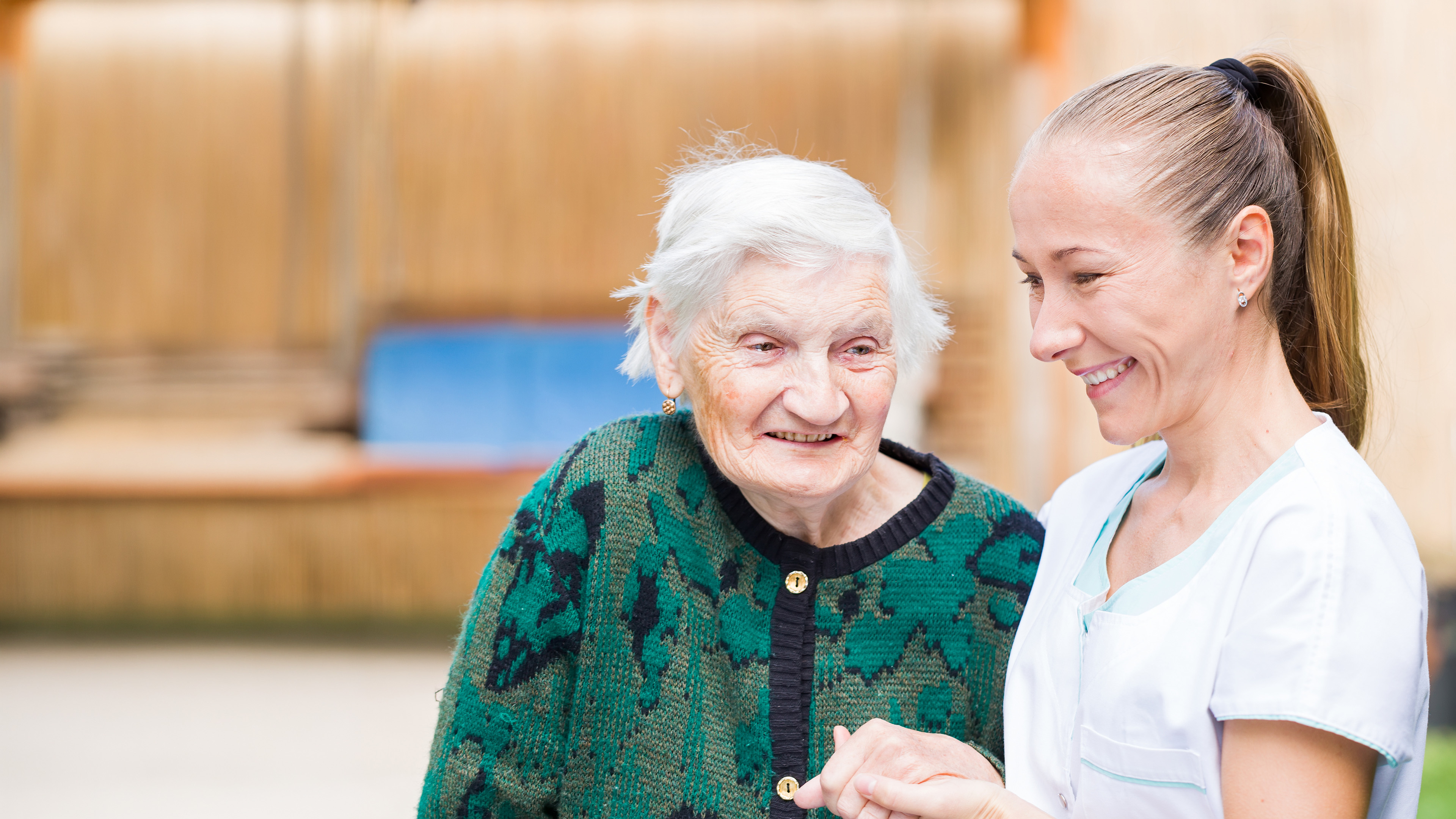 Pflegerin hält Seniorin an der Hand. Beide lächeln - KI unterstützt