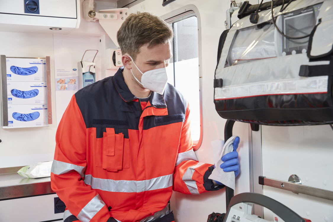 Rettungssanitäter desinfiziert den Griff der Rettungswagen-Tür mit einem Desinfektionstuch 