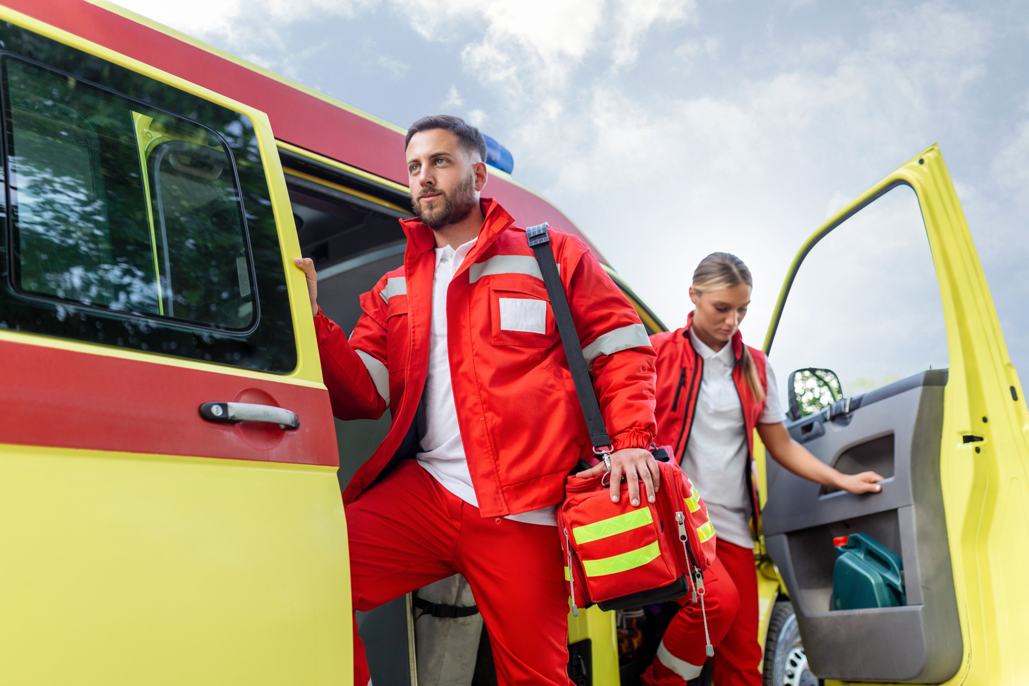 Rettungssanitäterin und Notarzt im Krankenwagen mit Ausrüstung. Ein Rettungssanitäter steht am Heck eines Krankenwagens bei den offenen Türen