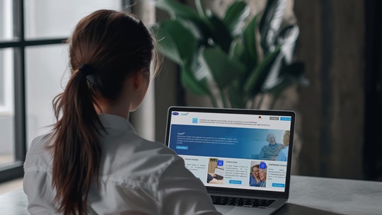 Frau sitzt vor Monitor auf der die Health+ App abgebildet ist