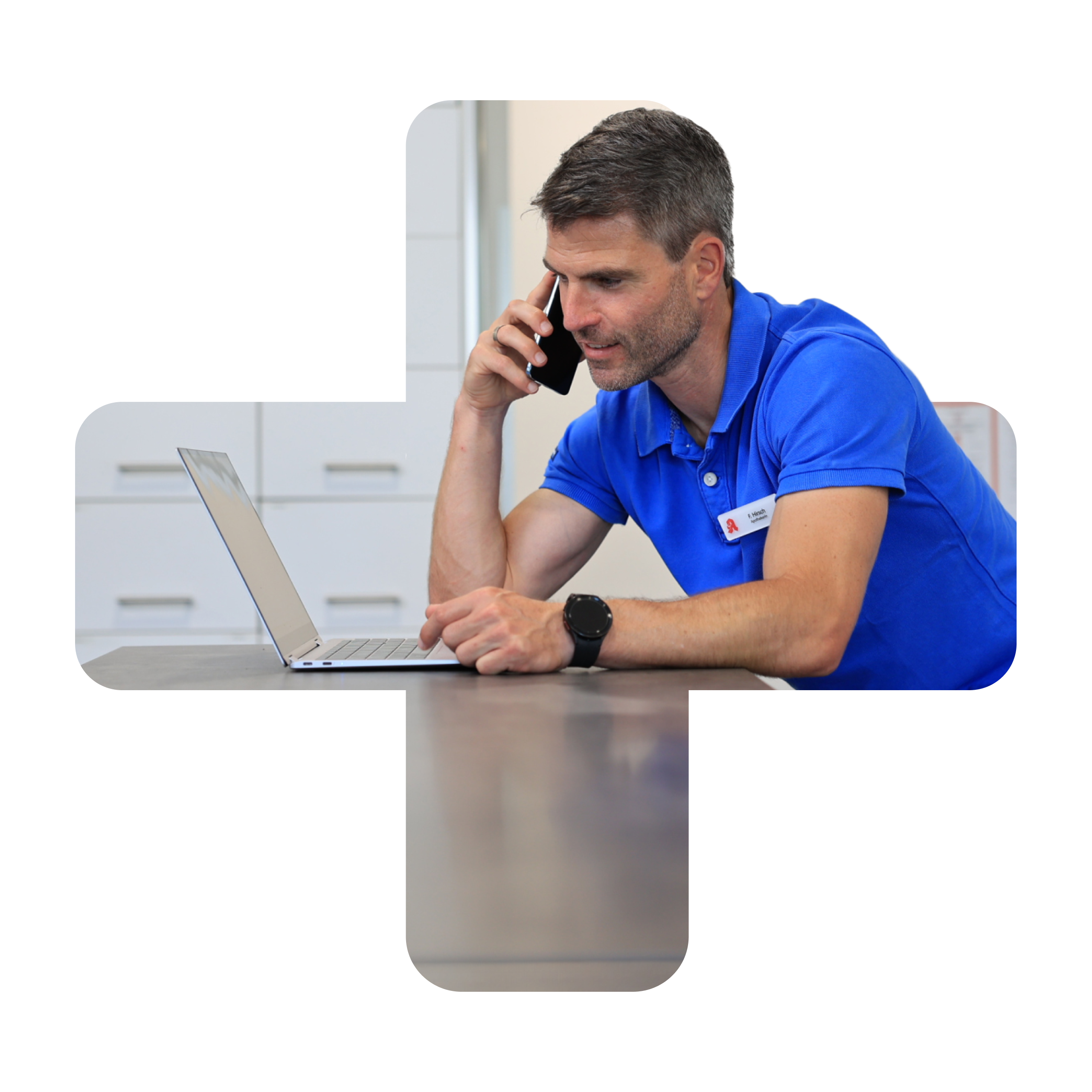 Apotheker in blauem Poloshirt telefoniert und blickt in einen Laptop, der auf dem Verkaufstresen steht.