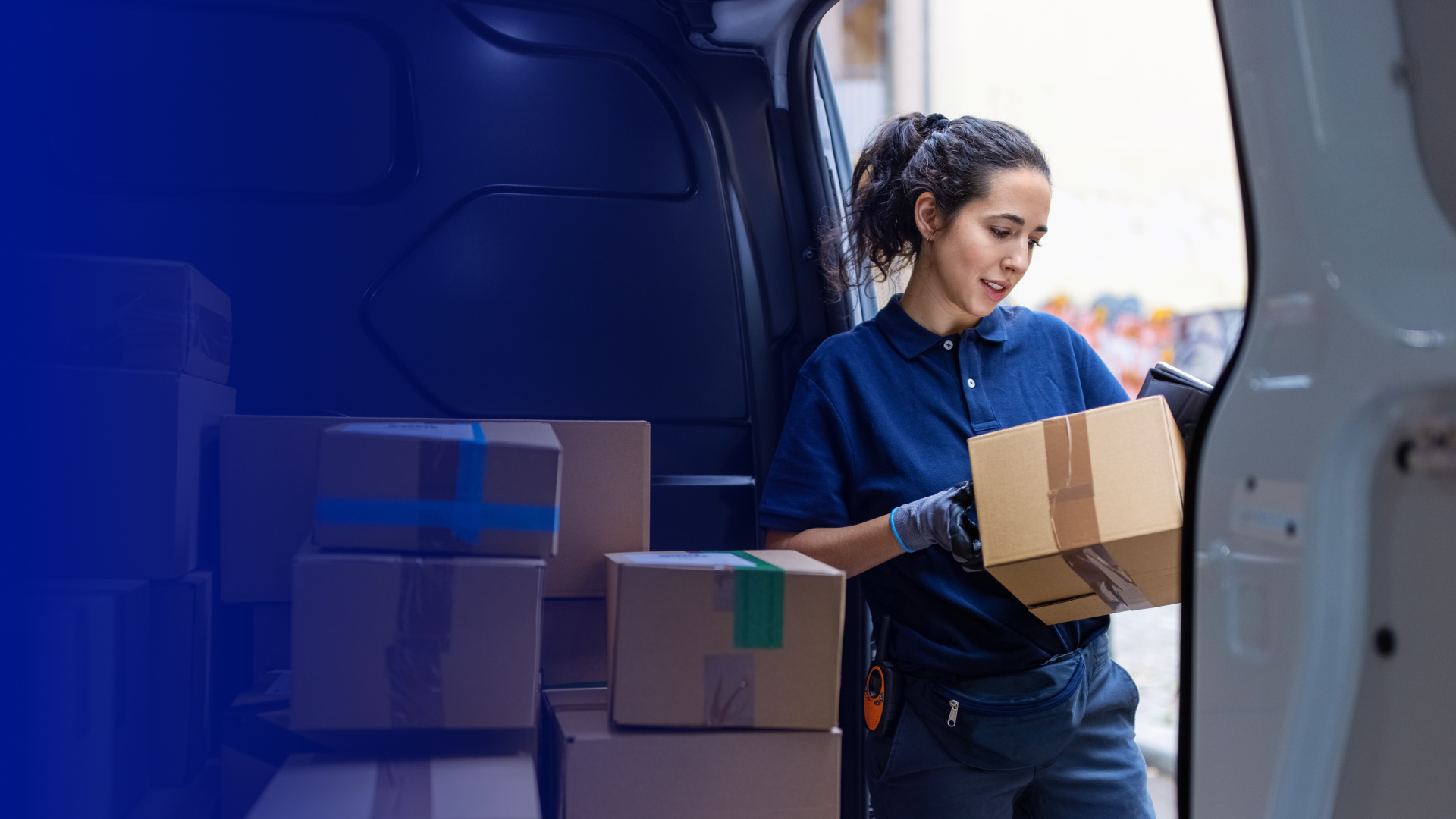 A young woman in a blue shirt unloads packages from a car.