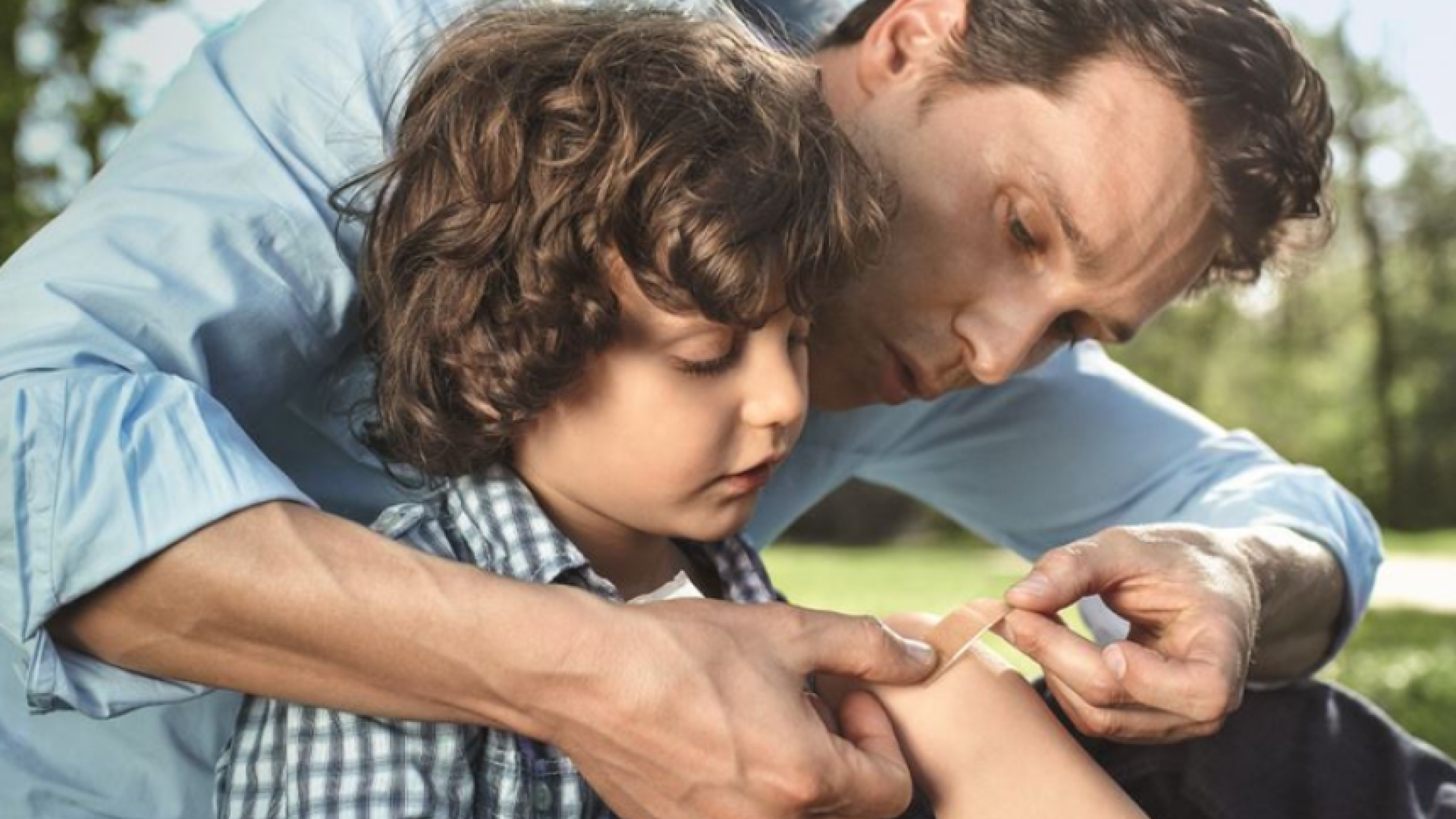 A father carefully sticks a plaster on his son's arm.