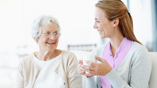 junge Frau hält Tasse in der Hand und unterhält sich mit Seniorin