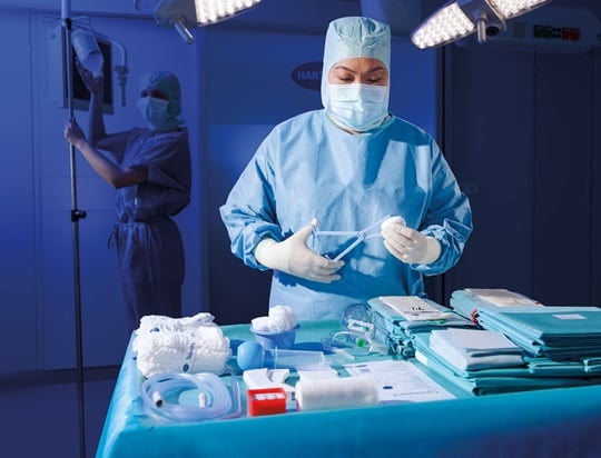 Medical staff in blue scrubs preparing surgical instruments on a tray under bright lights, ensuring precision and cleanliness in a sterile operating room environment.