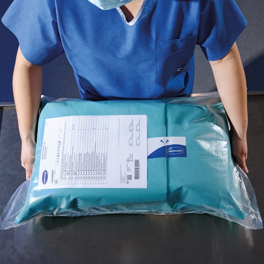 Person in blue scrubs holding a sealed medical drape pack with a checklist. The pack is designed for surgical use, emphasizing sterility and quality.