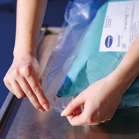 Close-up of hands carefully opening a clear plastic medical packaging containing a teal package labeled with product details.