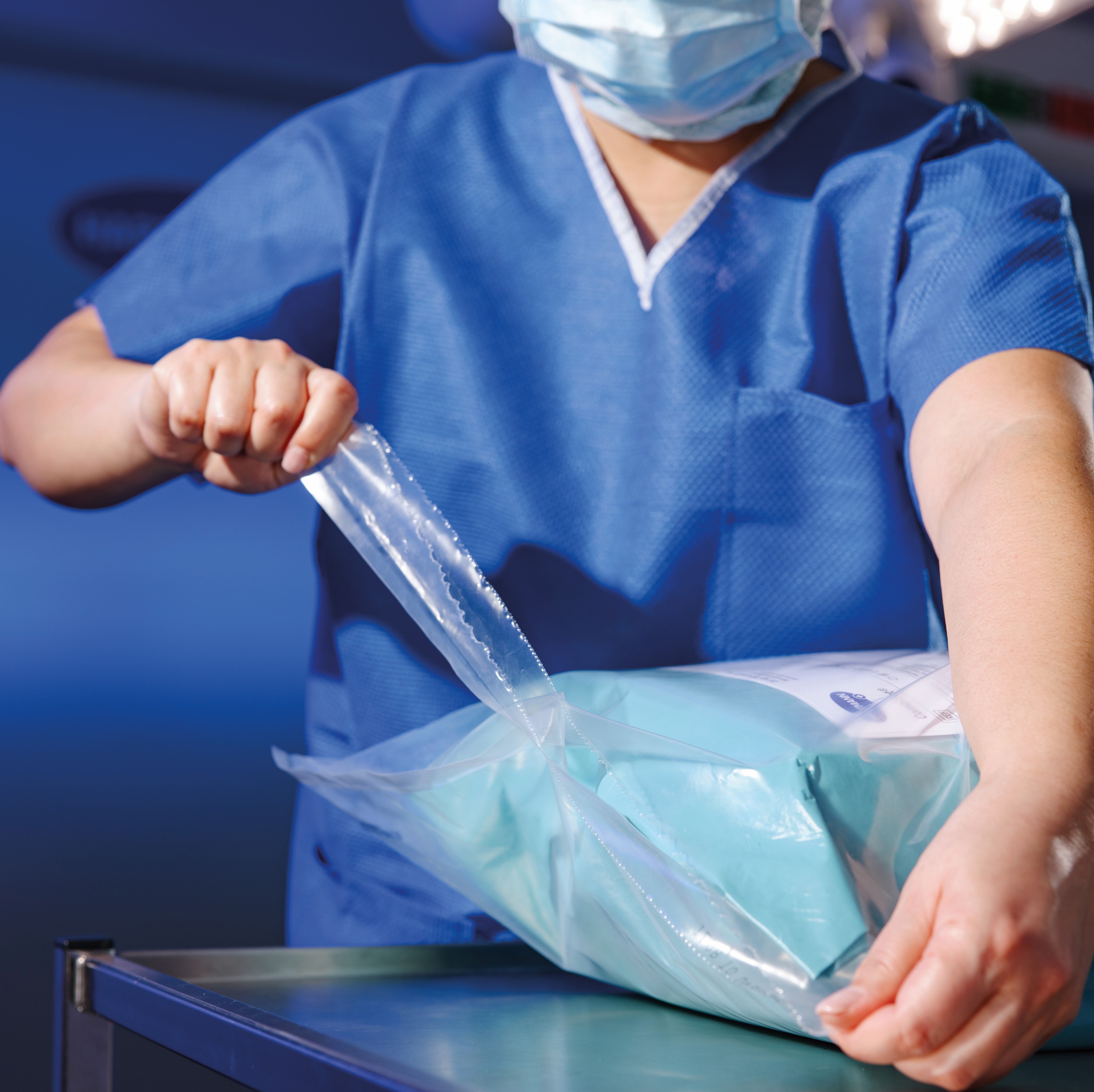Medizinische Fachkraft in blauer Kleidung öffnet auf einem Tisch eine transparente, versiegelte Verpackung mit sterilen Medizinprodukten.