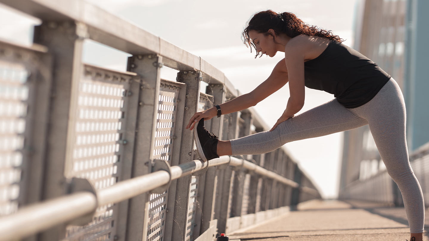 Woman stretching her leg on a bridge railing during a workout, highlighting flexibility, injury prevention, and active lifestyle.