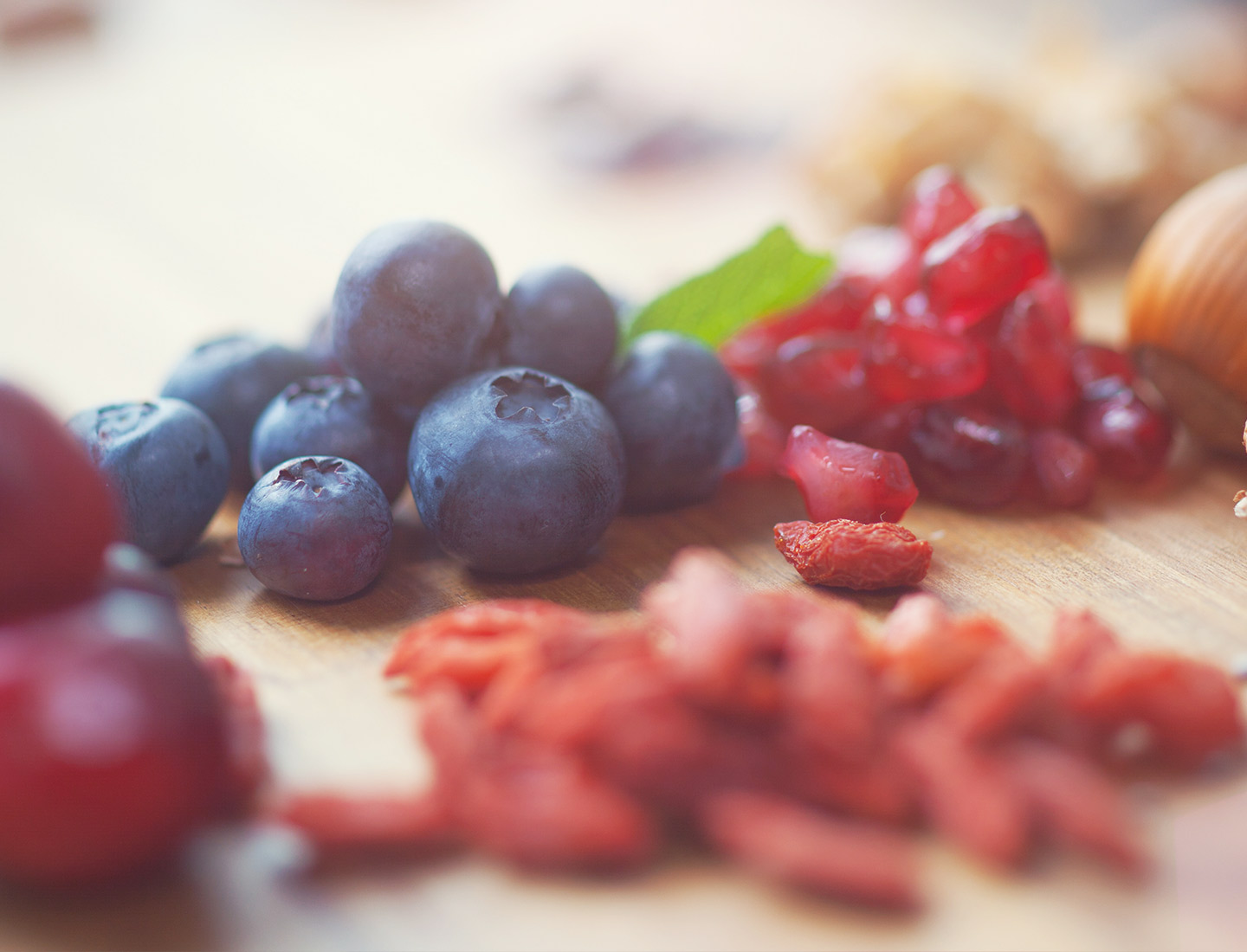 Close-up of fresh blueberries, pomegranate seeds, and goji berries on a wooden surface, representing healthy and natural nutrition.