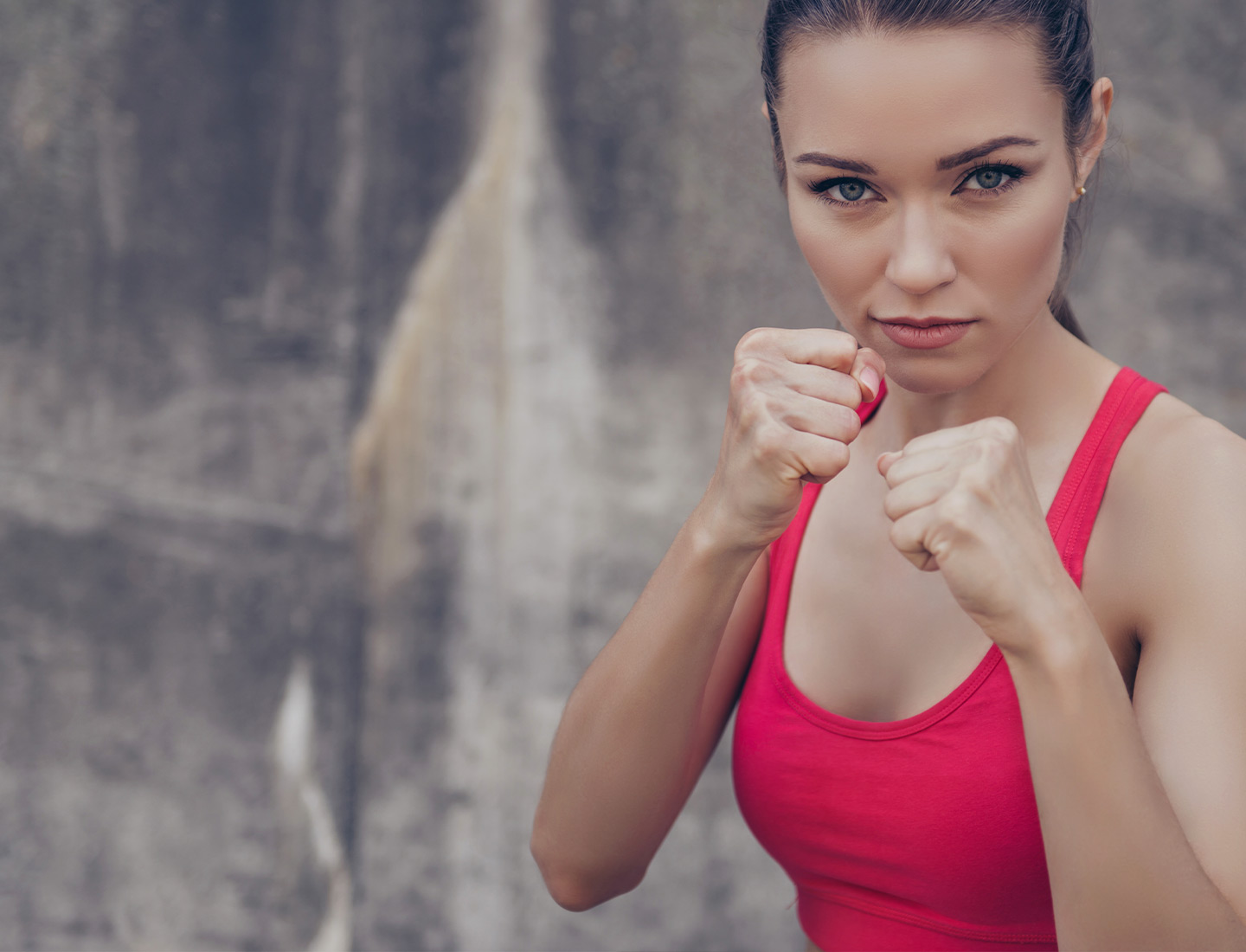 Confident athletic woman in red sportswear posing in a boxing stance, ready to fight, with a determined expression.