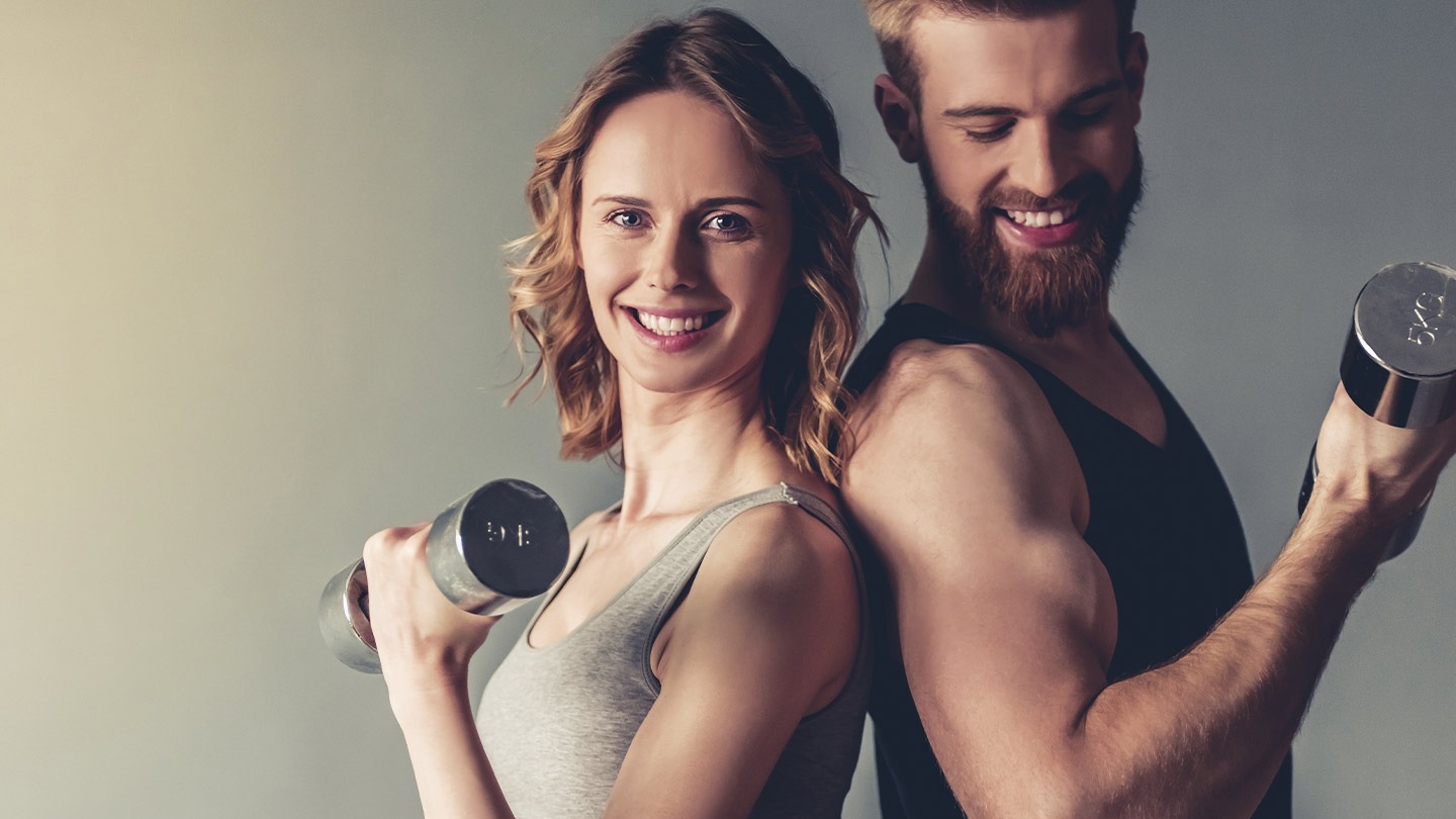 Smiling fit couple standing back-to-back holding dumbbells, showcasing active lifestyle and fitness training.