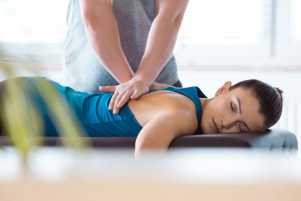 Woman lying face down on a massage table with eyes closed, receiving a back massage for relaxation and muscle recovery.