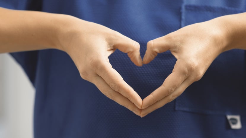 A nurse shapes a heart with their hands.