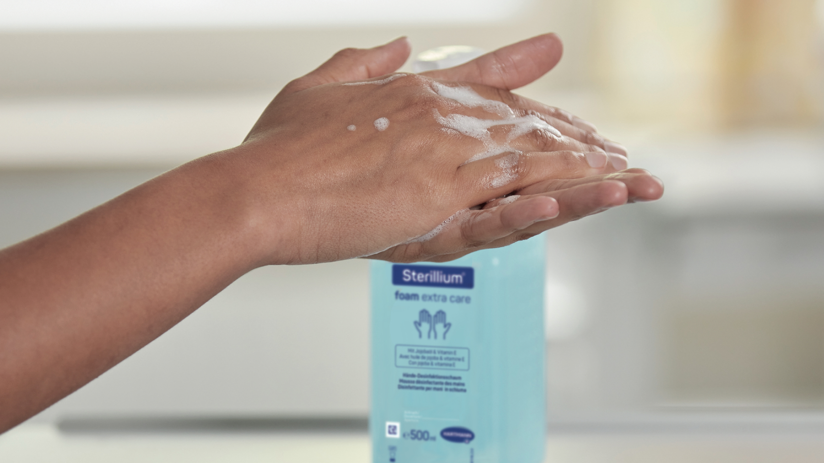  Nahaufnahme von Händen, die mit Seifenlauge bedeckt sind, vor einer Flasche Sterillium®.