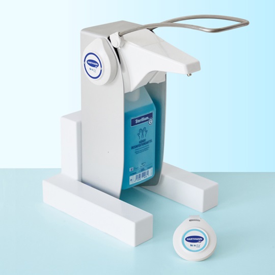 A white Sterillium® hand sanitizer dispenser with a blue liquid container and a white refill pod in front of it, both positioned on a light blue surface.