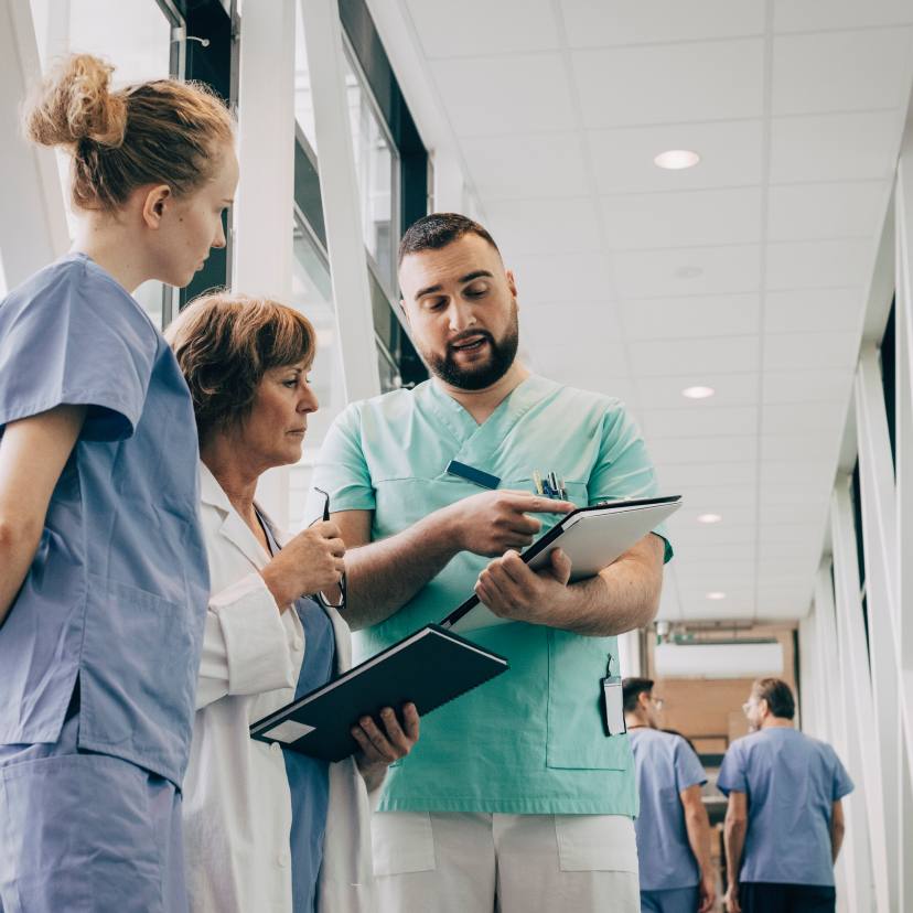 A male nurse shows something on a clipboard to two female nurses.