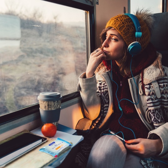 Girl on train, looking outside the window with her snacks on the table and a package of Sterillium® wipes in front of her.