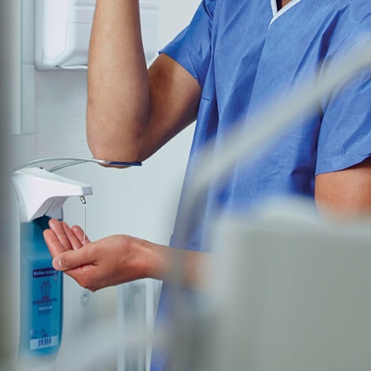 Doctor using a wall mounted Sterillium® dispenser with ellbow to apply on hands.