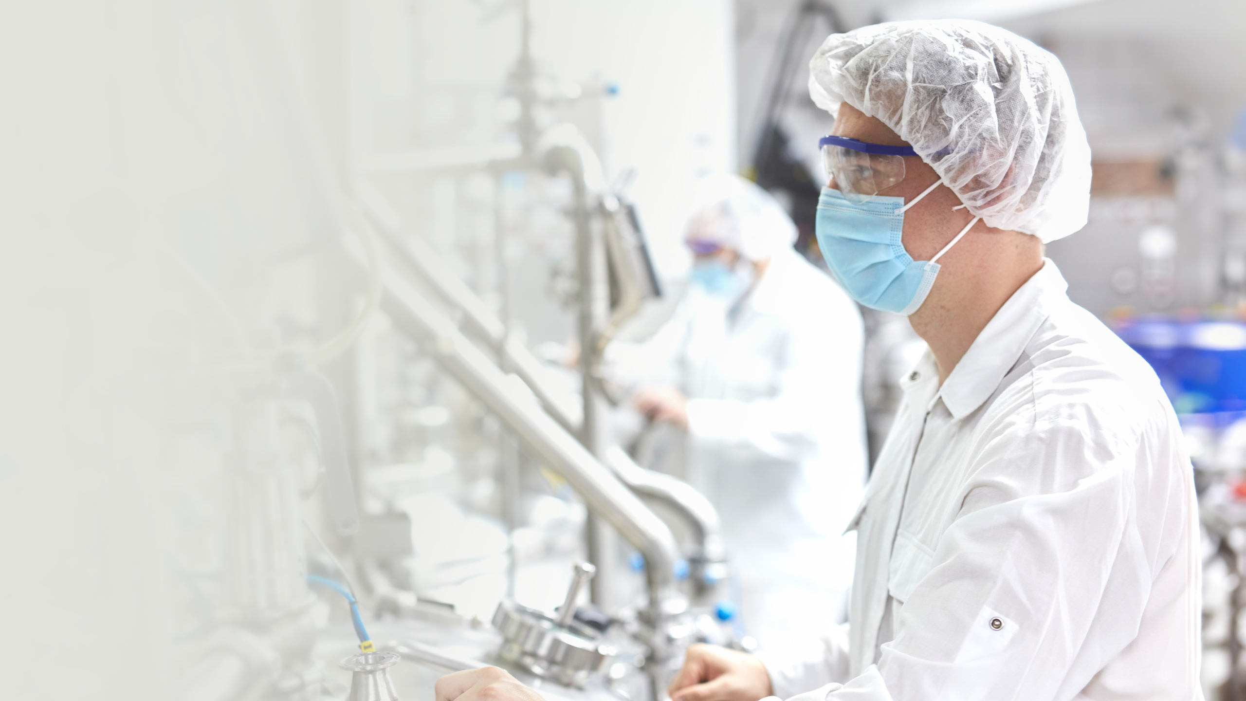 A doctor wearing a facemask, surgical hood, and plastic goggles operates a machine.