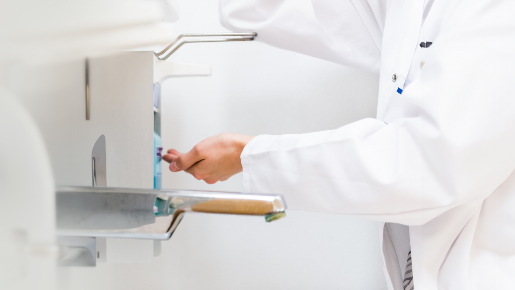 A hospital staff member in a white coat uses a Sterillium® hand sanitizer dispenser.