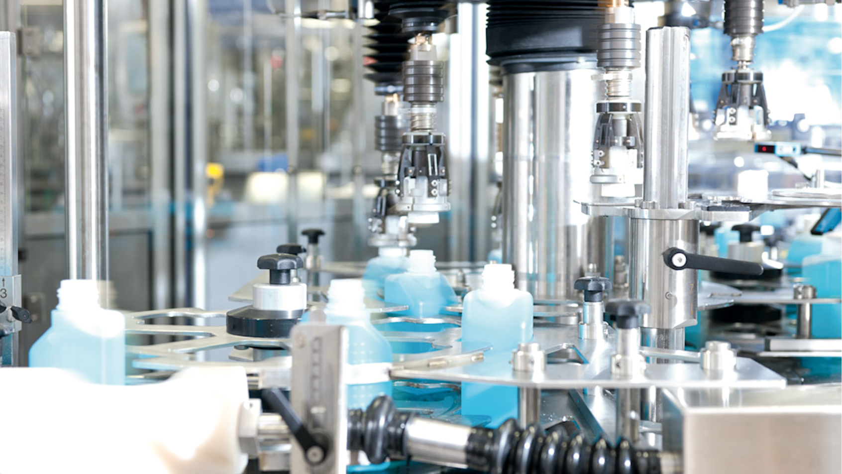 Plastic bottles being filled with blue liquid by machines in a factory.