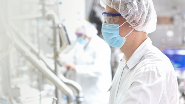 A doctor wearing a facemask, surgical hood, and plastic goggles operates a machine.