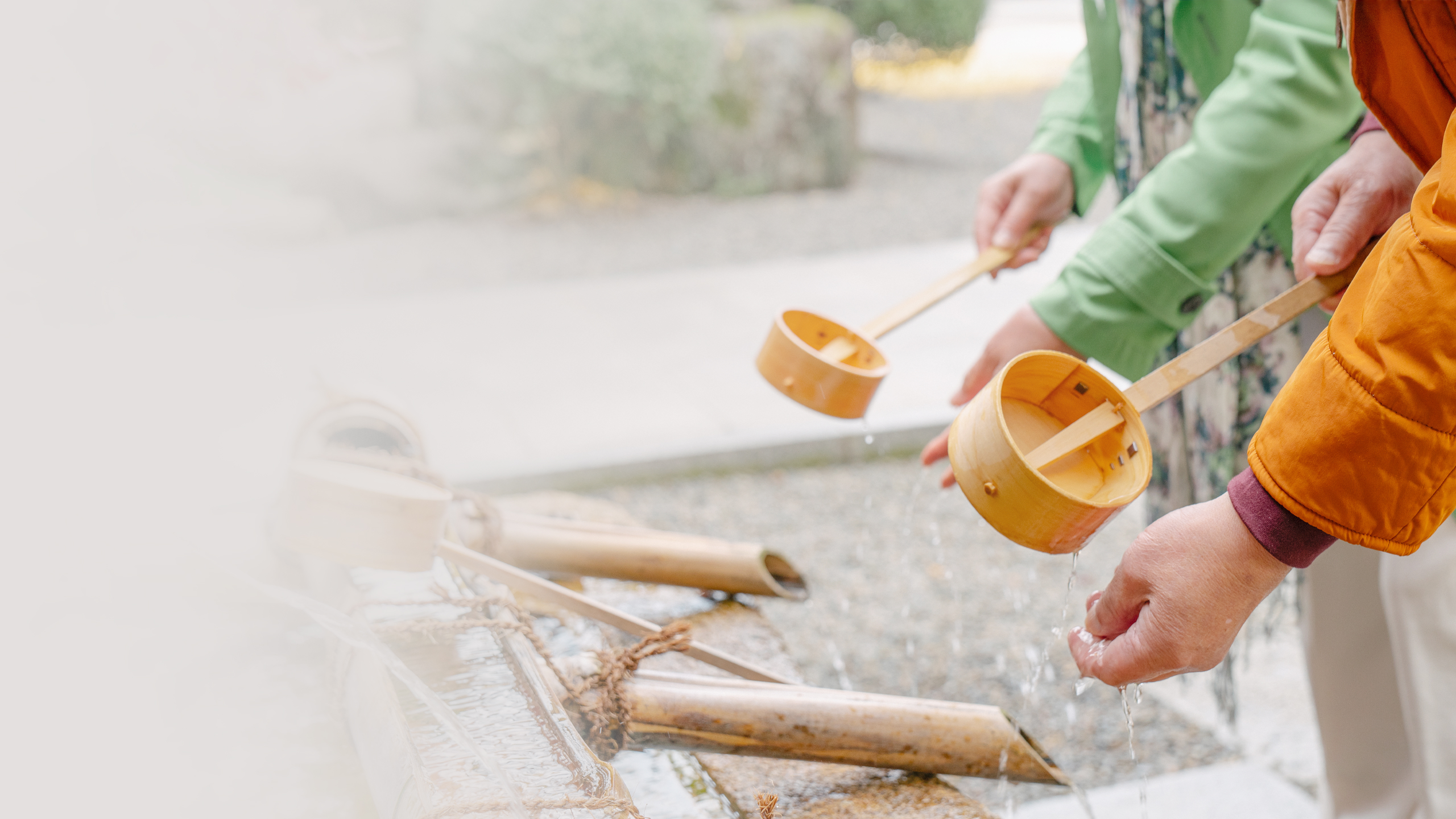 Two people wash their hands over a fountain, using a bamboo ladle.