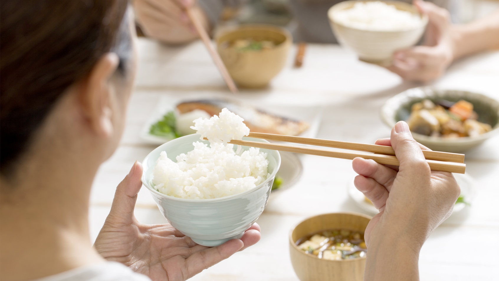 A woman eats a bowl of rice with chopsticks.