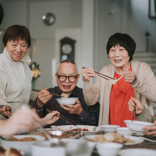 Three people at a dinner table eat dumplings with chopsticks.