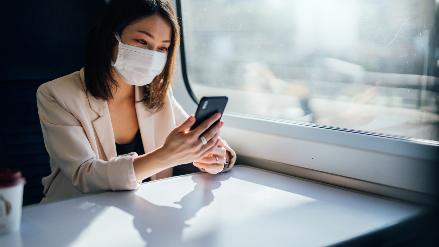 A woman wearing a facemask looks at her phone on the train.