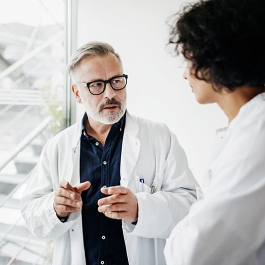 A male and a female doctor in white coats talk to each other.