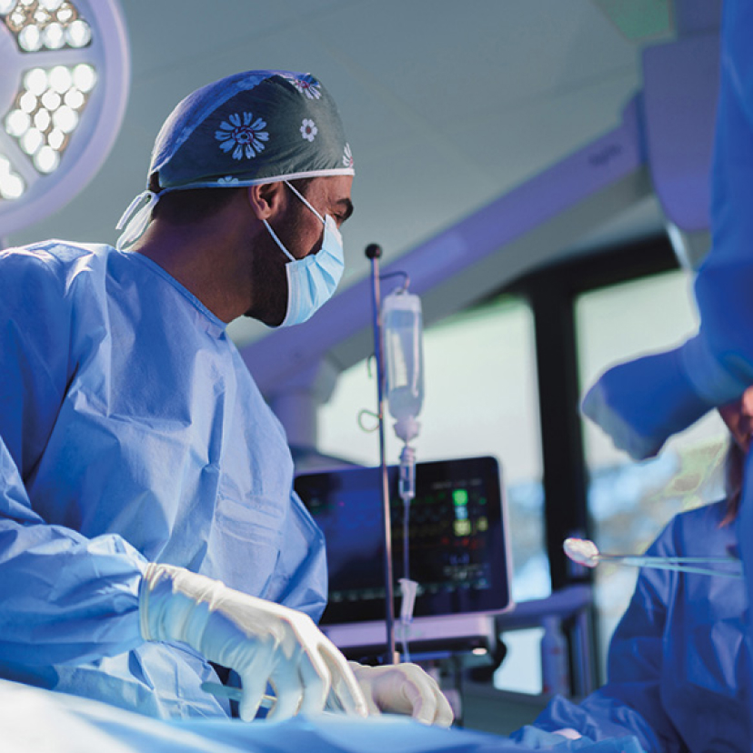 A doctor wearing a facemask and a surgical hood talks to a colleague during an operation.