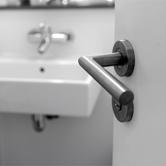 Black-and-white close-up of a door handle with a sink in the background.