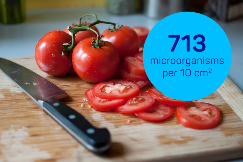 Tomatoes and a knife on a wooden cutting board with a tag that says 713 microorganisms per 10cm².