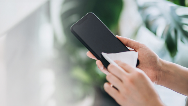 Someone wipes their phone screen with a tissue.