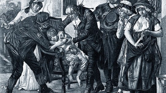 Historische Schwarz-Weiß-Zeichnung von Edward Jenner, der vor einer Gruppe von Menschen ein Kind impft.