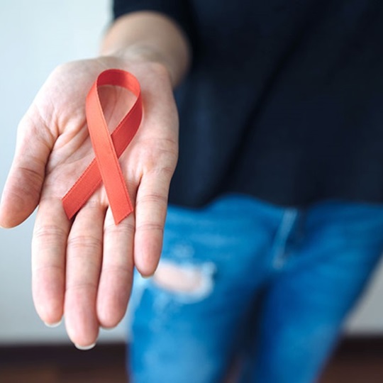 Rote HIV-Schleife in der Handfläche einer Person.