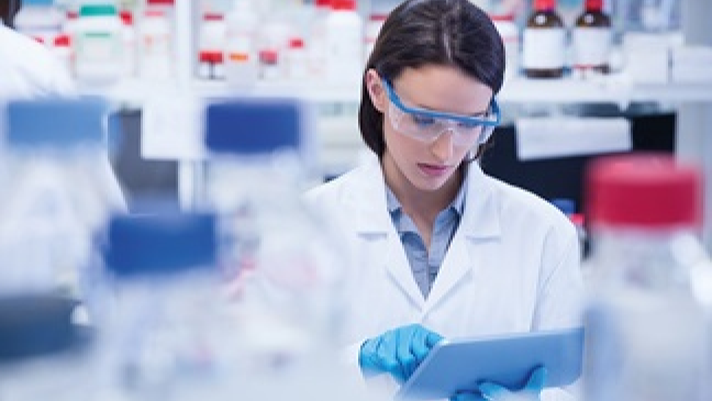 A scientist in a lab checks something on a clipboard.