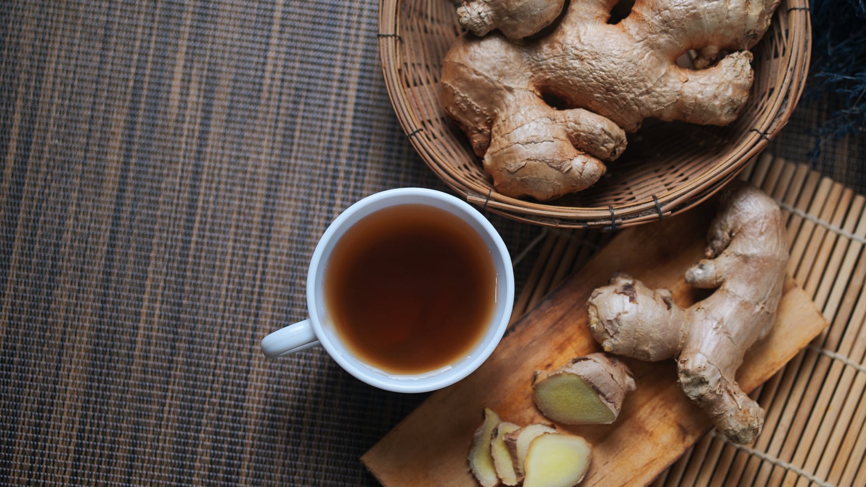 A cup of ginger tea with ginger roots next to it.