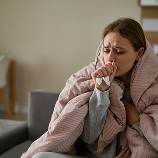 A woman with the ‘flu is coughing and is wrapped in a blanket.