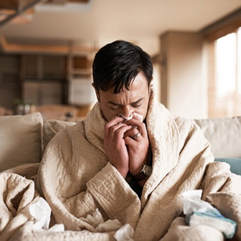 A man with the ‘flu wrapped in a blanket and blowing his nose.