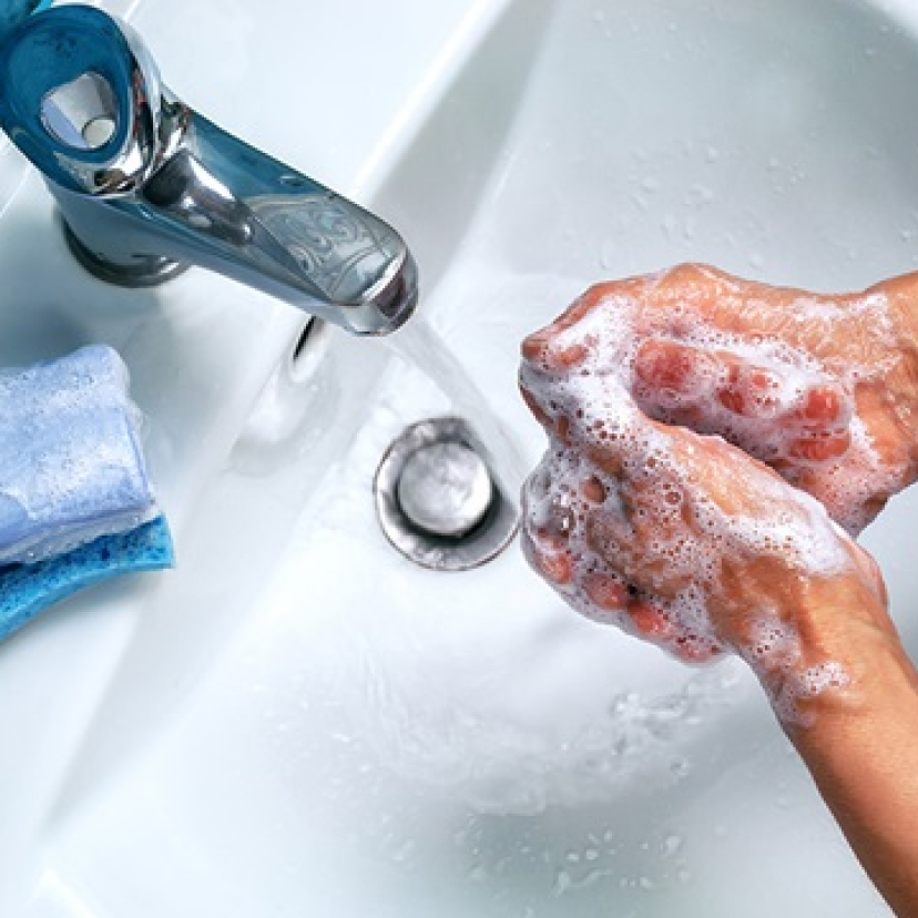 Person washing hands with soap under running water at a sink.