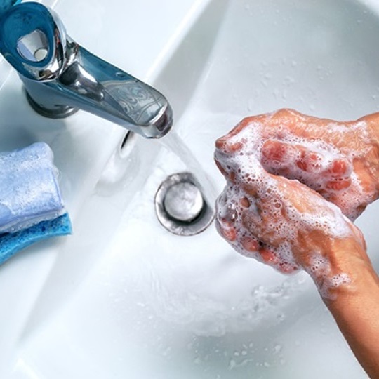 Person washing hands with soap under running water at a sink.